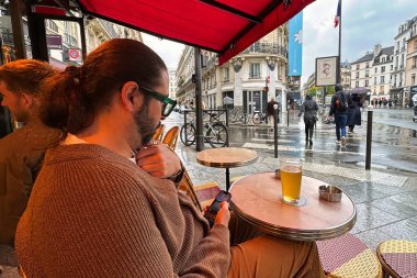 Paris, France - April 11 2023: a man is sitting at the table of a bar or restaurant on the sidewalk of a parisian street in the saint germain des pres neighborhood clipart