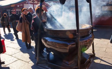 Tokyo, Japonya - 26 Kasım 2012: Asakusa ve Senso-ji tapınağı Tokyo 'da ziyaret edilen en yoğun ve en popüler yerlerden biridir. Burada kutsal bir yerde tütsü yakan bir kadın görüyoruz.