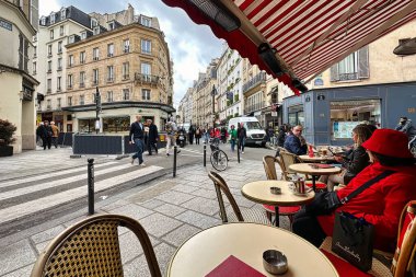 Paris, Fransa - 11 Nisan 2023: Saint Germain Pres Mahallesi 'nde bir Paris caddesinin kaldırımındaki bir bar veya restoranın masasında bir kadın oturuyor.