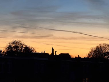 den haag, netherlands - November 04 2024: The sky displays beautiful colors at twilight with rooftops and trees silhouetted against the setting sun. clipart