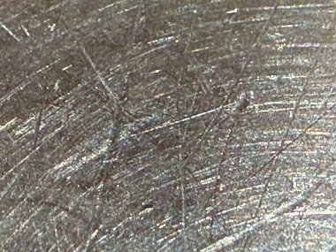 Detaylı bir yakın çekim görüntüsü, ışık altında çizik ve desenleri olan metalik bir maddenin dokulu yüzeyini gösterir..