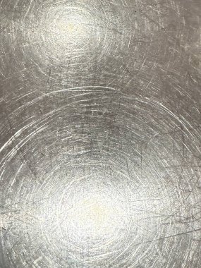 Metalik bir yüzey dairesel desenler ve parlak ve dokulu bir şekilde ışığı yansıtan çizikler gösterir..