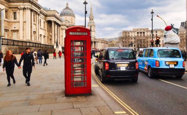 Londra, İngiltere - 6 Mart 2022: Londra 'da bir taksi geçmekte olan kırmızı bir İngiliz telefon kulübesinin önünden geçiyor ve arka planda ulusal galeri bulunuyor.