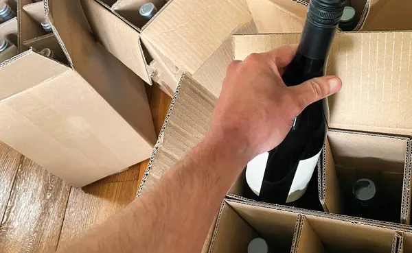 Birisi internetten sipariş edilen bir şişe şarabı bir teslimat kutusundan çıkarıyor.