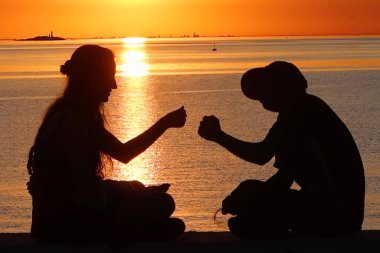 colonia del sacramento, uruguay - november 2 2022: two young people are giving each other a fist bump while enjoying the sunset over the ocean clipart