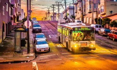 San Francisco, ABD - 07 Ocak 2013: Gün batımında Balboa Caddesi yakınlarında bir otobüs park halindeki arabalara ve elektrik hatlarına sıcak ışık tutuyor.