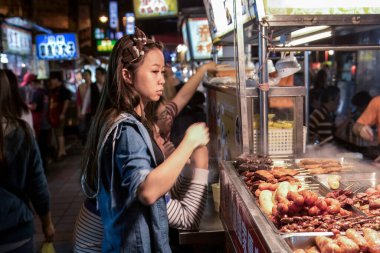 Taipei, Tayvan - 30 Kasım 2016: Bir kadın, akşam saatlerinde canlı piyasa faaliyetleriyle çevrili Taipei 'de hareketli bir sokak tezgahında yemek hazırlıyor.