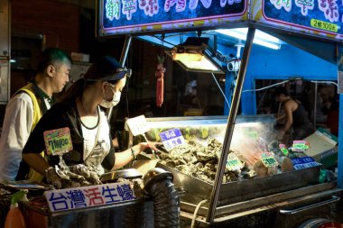 Taipei, Tayvan - 30 Kasım 2016: Bir Taipei gece pazarında bir satıcı neon ışıkları ve hevesli müşterilerle dolu hareketli bir atmosferde taze istiridye hazırlıyor.