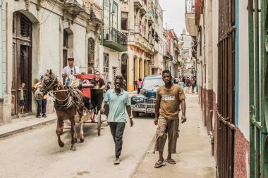 Havana, Küba - Temmuz 06 2018: Havana 'da canlı bir cadde boyunca yürüyen iki adam, bir at arabasının şehrin canlı atmosferini göstererek geçişi sırasında.