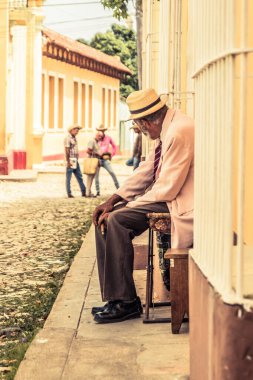 Trinidad, Küba - 15 Temmuz 2018: Trinidad Küba 'da bir kaldırım taşı caddesi boyunca bir sandalyede oturan yaşlı bir beyefendi. Caddede renkli binalar var..