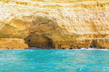 Albufeira, Portekiz - 20 Ocak 2016: Turkuaz sular Albufeira Algarve 'nin engebeli uçurumlarına nazikçe çarpıyor. Güneş ışığı mağara girişini aydınlatıyor..