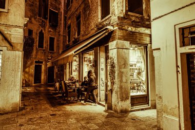 Venedik, İtalya - 16 Şubat 2016: Bir çift sıcak akşam ışıkları altında sessiz bir Venedik caddesi yakınlarındaki açık bir kafede içki içiyor.