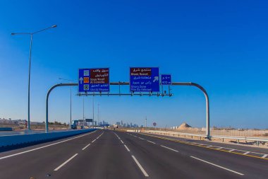 Doha, Katar - 28 Ocak 2010: Uzakta mavi gökyüzü ve şehir manzarasıyla Doha şehir merkezine doğru giden bir otoyol tabelasının net bir görüntüsü.