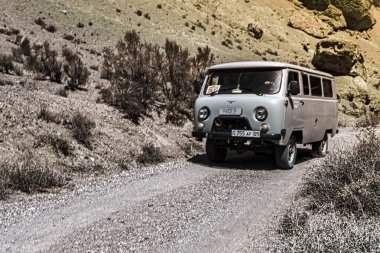 Almaty, Kazachstan - 16 Haziran 2017: Klasik bir minibüs çarpıcı dağ arazisi ve doğal güzelliklerle çevrili çakıl yolu Charyn kanyonu boyunca sürüyor.