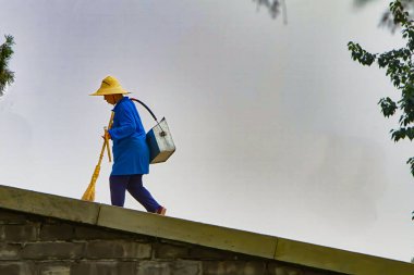 Pekin, Çin - 18 Temmuz 2010: Mavi elbiseli ve hasır şapkalı bir kişi bulutlu bir günde Pekin 'deki yüksek bir duvardan enkazı temizliyor.