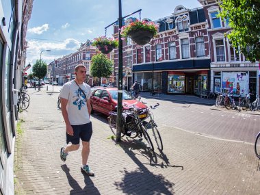 Lahey, Hollanda - 30 Mayıs 2009: Açık tenli bir adam, güneşli bir günde Hollanda 'nın Den Haag şehrinde park halindeki bisiklet ve arabaların yanından geçen bir kaldırımda yürüyor.