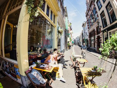 Den Haag, Hollanda - Haziran 02 2009: İnsanlar Den Haag 'da güneşli bir günde açık kafe masalarında oturuyorlar. Caddede bir bisikletçi geziniyor..