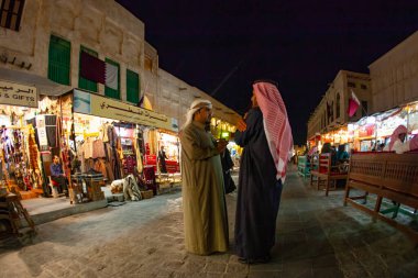 Doha, Katar - 28 Ocak 2010: İki erkek sıcak akşam ışıkları altında Doha Katar 'daki geleneksel bir pazarın canlı dükkanlarını keşfederken sohbet ediyorlar.