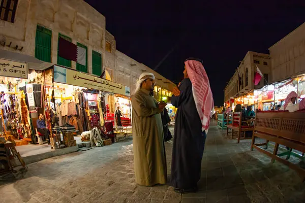 Doha, Katar - 28 Ocak 2010: İki erkek sıcak akşam ışıkları altında Doha Katar 'daki geleneksel bir pazarın canlı dükkanlarını keşfederken sohbet ediyorlar.