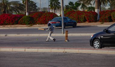 Doha, Katar - 26 Ocak 2010: Doha Katar 'da genç bir çocuk açık mavi gökyüzünün altındaki boş bir otoparkta kriket maçının keyfini çıkarıyor.