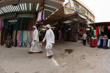 Kuveyt Şehri, Kuveyt - 24 Şubat 2010: İki adam Kuveyt 'teki hareketli bir pazarda renkli kumaş tezgahlarının yanından geçerek gün boyunca yerel kültürü sergilediler.