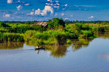 Bago, Myanmar - Aralık 03 2012: Yalnız bir balıkçı Myanmar 'da yemyeşil yemyeşil ve açık mavi gökyüzü ile çevrili sakin bir nehirde yol alır..