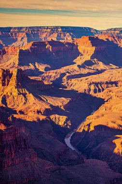 Görkemli kaya oluşumları ve altın günbatımı ışığıyla aydınlatılan derin kanyonlar manzaranın üzerine uzun gölgeler salıyor..