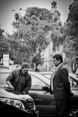 Lima, Peru - August 12 2010: A driver in a suit oversees a car wash on a busy street in Lima while casually watching the worker clean his vehicle. clipart