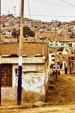Lima, Peru - 13 Ağustos 2010: Peru 'da bir gecekondu kasabasında basit binalar ve uzak yamaçlardaki evlerle çevrili toprak bir yolda iki kişi yürüyor.