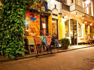 Lahey, Hollanda - Haziran 05 2009: Bisiklet gece dışarıda renkli sandalyeli bir kafe yakınında dinleniyor. İnsanlar oturup yemek yiyor. Hollanda 'nın Den Haag şehrinde yer almaktadır..