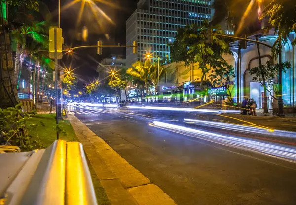 Honolulu, Amerika Birleşik Devletleri, 07 Aralık 2012: Waikiki 'de yoğun bir cadde boyunca trafik hızla ilerliyor parlak ışıklarla aydınlatılıyor ve geceleri palmiye ağaçları ile çevriliyor.