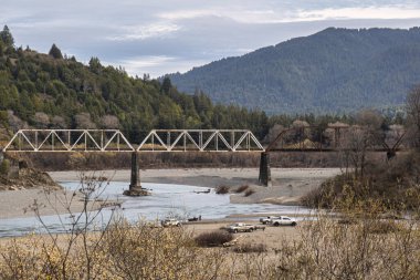 Garberville, ABD - 15 Şubat 2020: Eski bir çelik köprü Garberville California 'daki gür ağaçlarla çevrili geniş bir dağ nehrini geçer