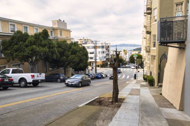 San Francisco, ABD - 14 Şubat 2020: Tipik San Francisco caddesi Viktorya dönemi evleri dik eğimli ve bulutlu bir günde park edilmiş arabalar.
