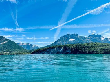 Menthon St. Bernard, Fransa - Eylül 06: 2024 Annecy 'deki görkemli dağlarla çevrili berrak mavi gökyüzünü yansıtan sakin turkuaz suların nefes kesici görüntüsü. Huzurlu atmosfer davet ediyor