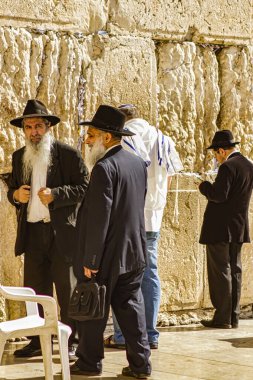 Kudüs, İsrail - 12 Kasım 2010: Ziyaretçiler geleneksel giyinmiş erkeklerin ruhani bir atmosfer yarattığı Kudüs Batı Duvarı 'nda namaz kılıyor ve yansıtıyorlar.