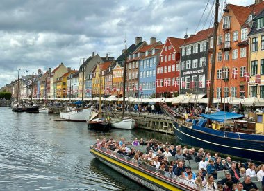 Kopenhag, Danimarka - 24 Temmuz 2023: Kalabalık renkli evler ve teknelerle dolu Nyhavn limanını keşfederken yaz günlerinde tekne turlarının keyfini çıkarıyor.