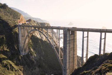 Big Sur, ABD - 19 Şubat 2020: Büyük Sur 'un panoramik görüntüsü, engebeli kıyı şeridi ve okyanus dalgaları karşısında Bixby Köprüsü' nü sergiliyor.