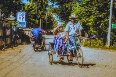 Bago, Myanmar - 02 Aralık 2012: Bir adam Myanmar 'da kırsal bir yolda, arkasında oturan yaşlı bir kadınla birlikte sakin bir çevrede bisiklet sürüyor..