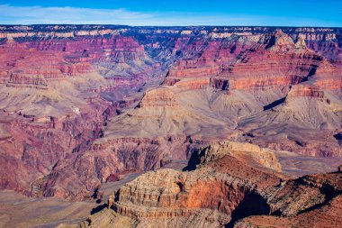 Arizona 'daki Büyük Kanyon' un nefes kesici manzarası açık mavi gökyüzünün altında renkli kaya oluşumları ve derin kanyonlar sergiliyor..