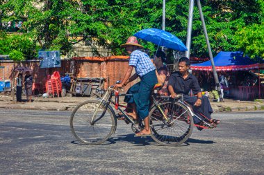 Yangon, Myanmar - 03 Aralık 2012: Bir bisikletçi Yangon 'da bir şemsiye altında bir yolcuyu naklederek Myanmars' ın hareketli sokaklarında günlük yaşamı yakalıyor.