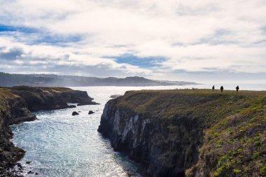 Mendocino, ABD - 16 Şubat 2020: Ziyaretçiler bulutlu bir gökyüzü altında dalgaların kayalık kıyılara çarpmasıyla Mendocino 'nun kayalıklarını ve körfezlerini keşfediyorlar.