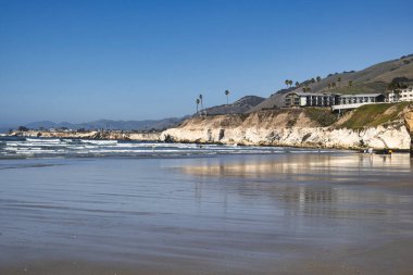 Pismo Beach, ABD - 19 Şubat 2020: Pasifik Okyanusu üzerinde kayalar ve beyaz kayalıklar yükselirken, açık bir Şubat günü kumsalda hafif dalgalar tur atar..