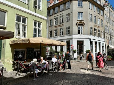 Kopenhag, Danimarka - 25 Temmuz 2023: Güneşli bir günde insanlar Kopenhag 'ın eski merkezinin büyüleyici tarihi caddesinde bir terasta sosyalleşiyorlar..