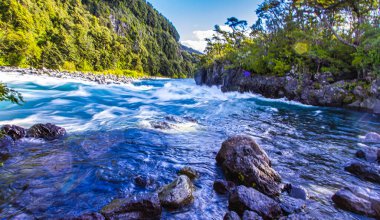 Vahşi Petrohue Nehri, Puerto Varas Şili 'deki yemyeşil dağlar ve ağaçlarla çevrili kayaların üzerinde dramatik bir şekilde çağlıyor..