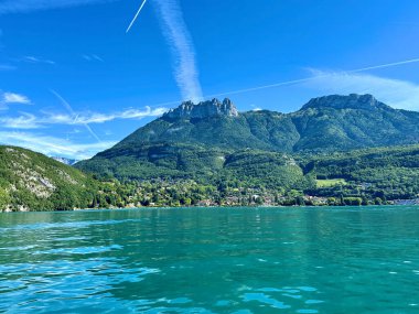 Menthon st. Bernard, Fransa - Eylül 06: 2024: Annecy Gölü 'nün sakin suları, arka planda yemyeşil ve görkemli dağlar tarafından çerçevelenerek barışçıl bir doğal ortam yaratıyor.