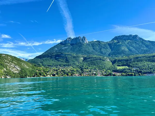 Menthon st. Bernard, Fransa - Eylül 06: 2024: Annecy Gölü 'nün sakin suları, arka planda yemyeşil ve görkemli dağlar tarafından çerçevelenerek barışçıl bir doğal ortam yaratıyor.