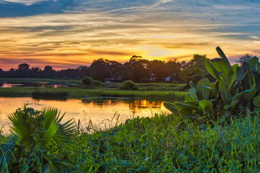 Yangon, Myanmar - 03 Aralık 2012: Berrak yeşillik ve sakin sularla çevrili Yangon Myanmar 'daki sakin nehrin üzerinde sakin bir günbatımı gökyüzünü resmediyor.