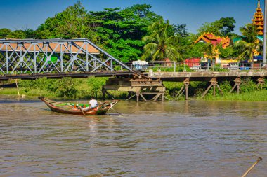 Yangon, Myanmar - 03 Aralık 2012: Yerel bir kürek Yangon 'da bir köprünün yanında ahşap bir tekne, yemyeşil ağaçlar ve canlı bir arkaplan oluşturur..