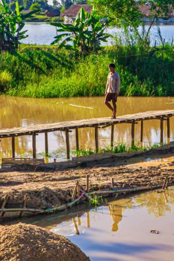 Bago, Myanmar - 03 Aralık 2012: Bir adam Myanmar 'ın kırsal kesimindeki çamurlu su üzerindeki ahşap bir köprüde gün ortasında dikkatle yürüyor.