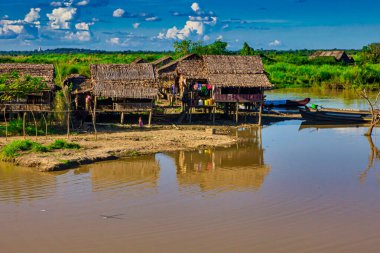 Bago, Myanmar - 03 Aralık 2012: Myanmar 'da yemyeşil ve açık mavi gökyüzü ile çevrili nehir kenarındaki sazlıklar üzerinde köy evleri duruyor.